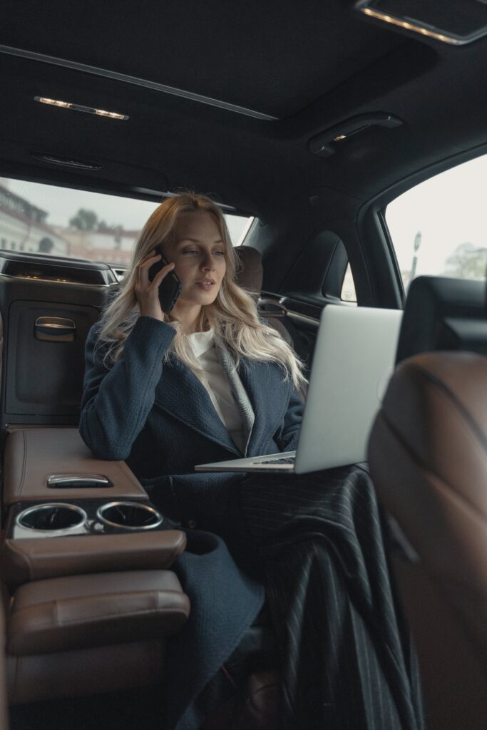 Powerful woman CEO working on a laptop while on a phone call in a luxurious car