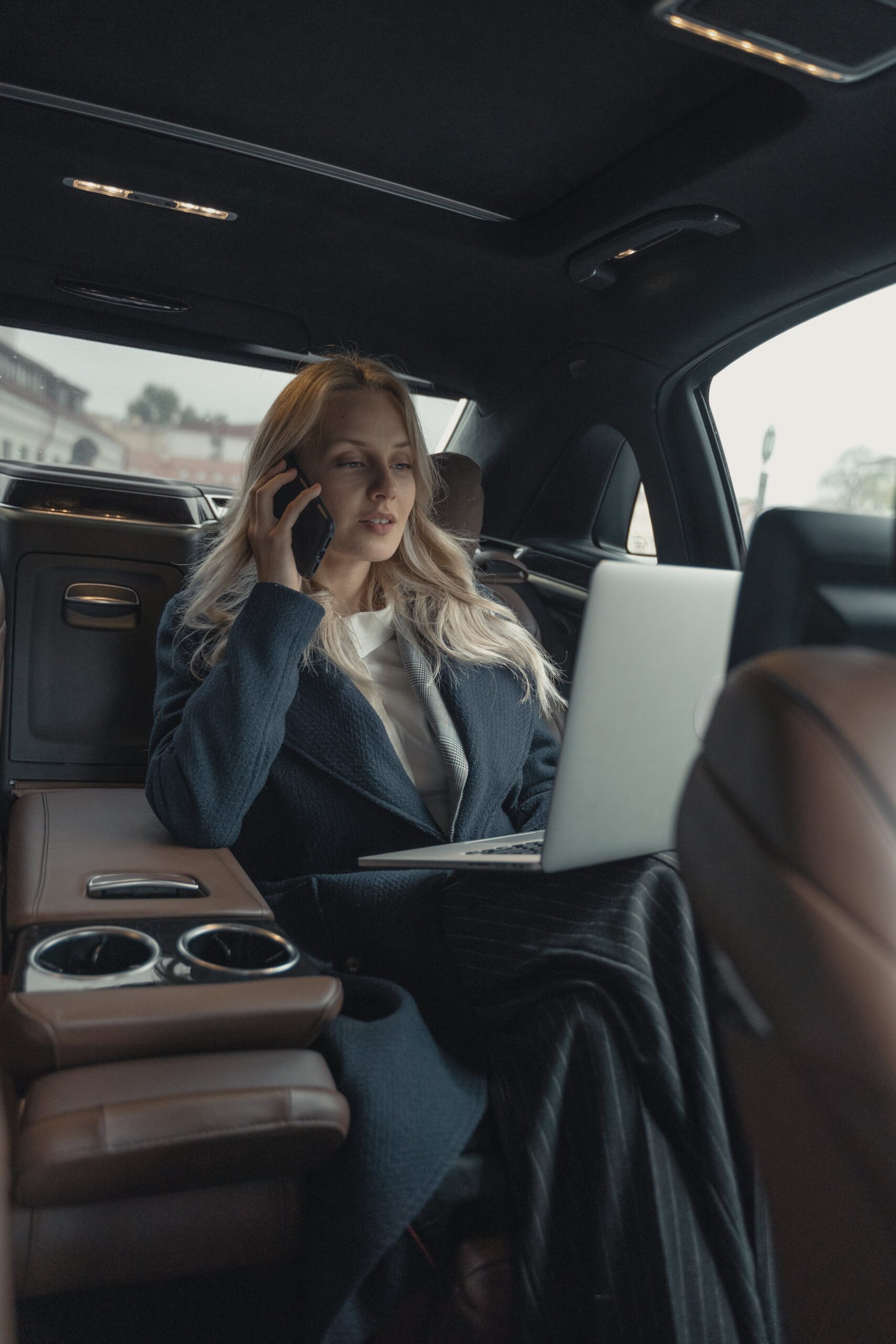Powerful woman CEO working on a laptop while on a phone call in a luxurious car
