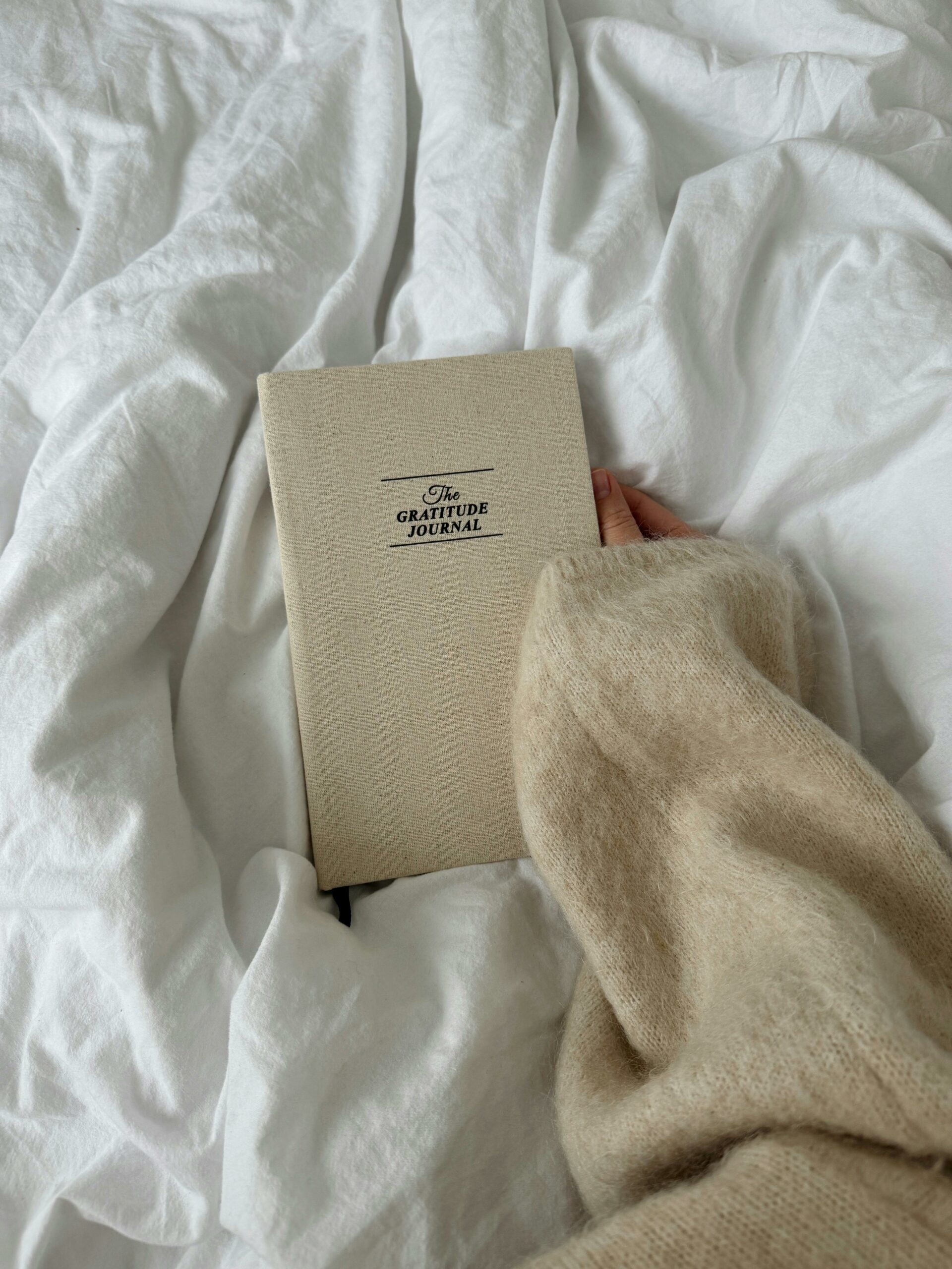 A person holding a gratitude journal on a bed, symbolizing the practice of daily gratitude.